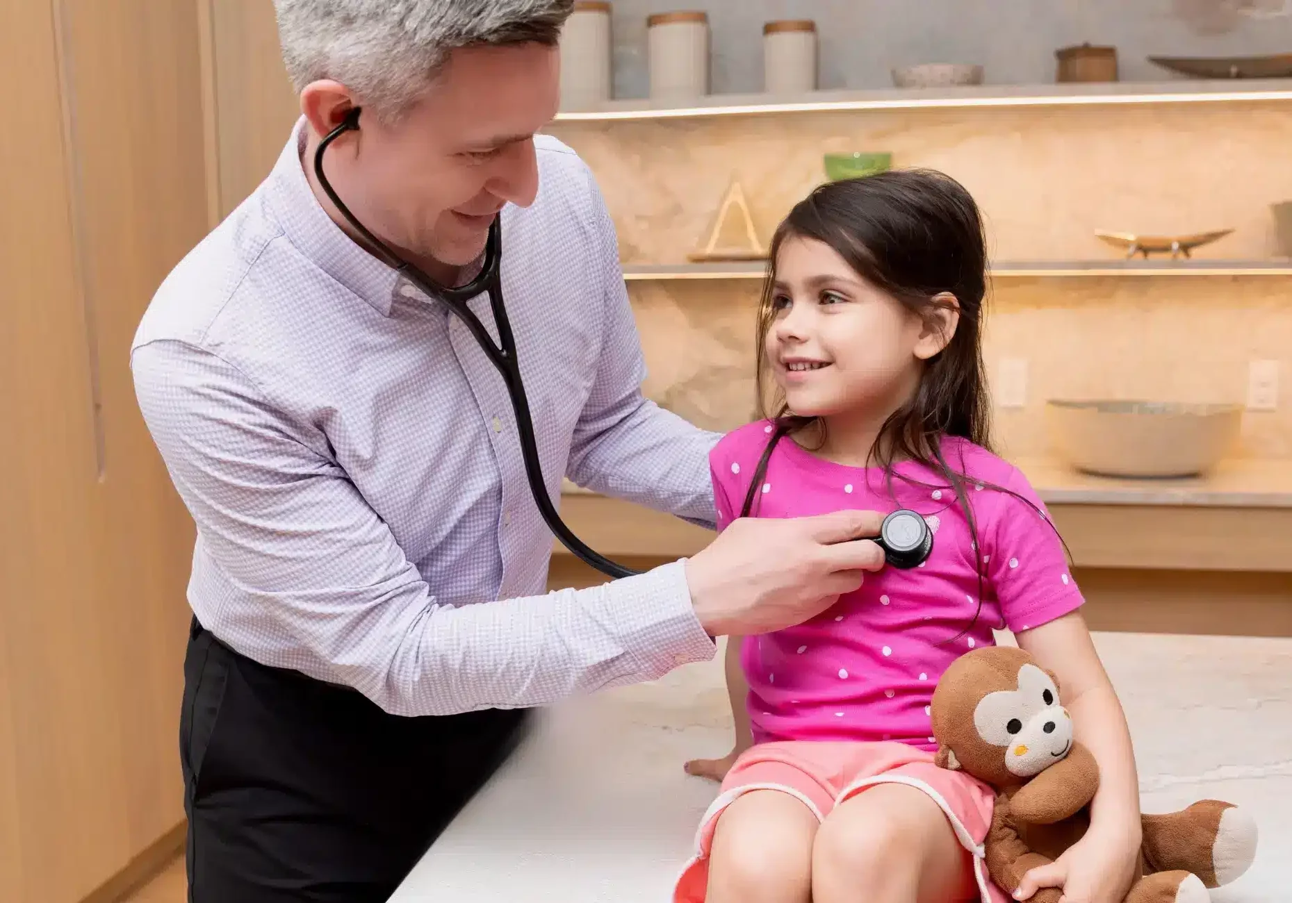 Dr Elliston checking 5 year old girls heartbeat with a stethoscope in New York City apartment kitchen smiling